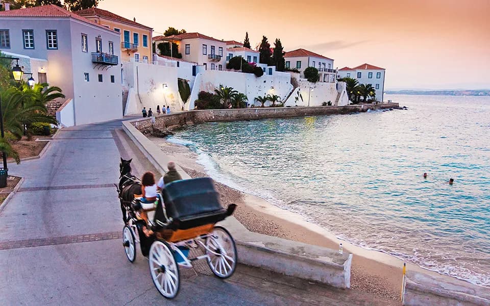 Πανοραμική θέα του παραλιακού μετώπου των Σπετσών στο ηλιοβασίλεμα με παραδοσιακή άμαξα